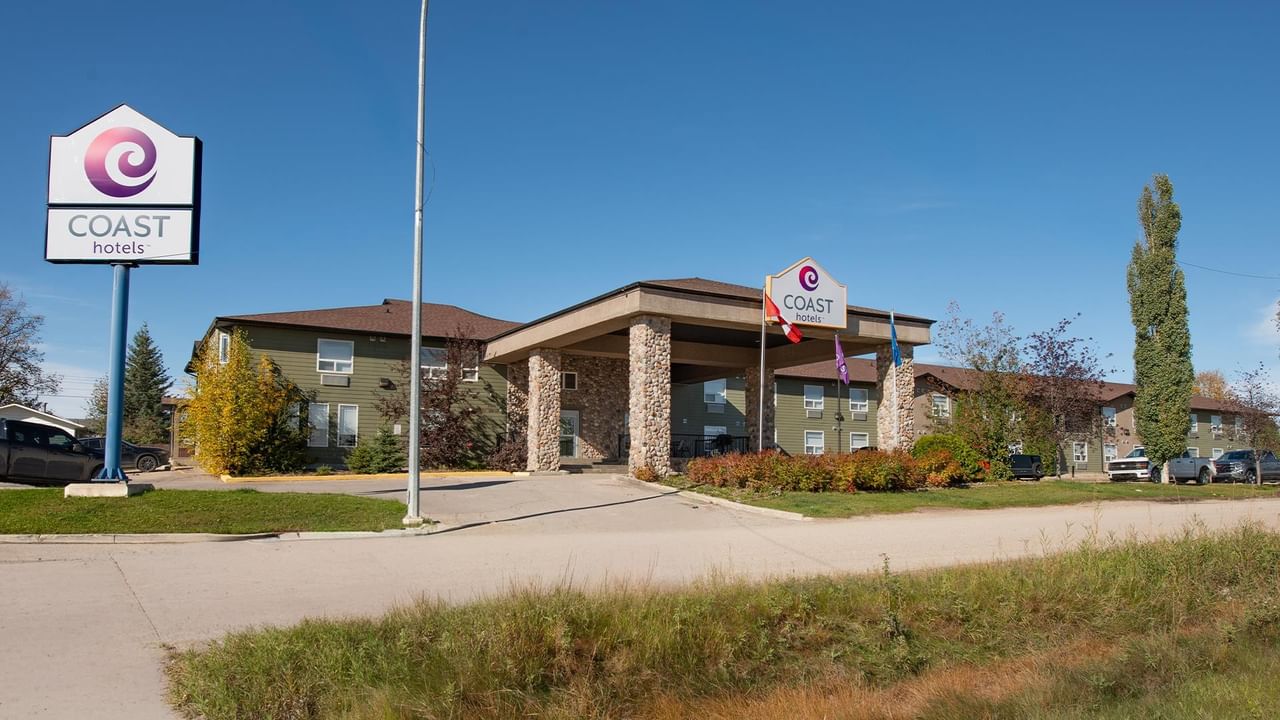 Modern hotel exterior with stone pillars, covered entrance, and Coast Hotels branded signage under clear blue sky.