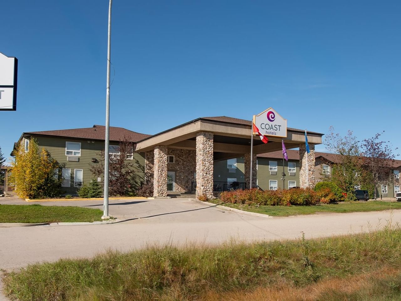 Modern hotel exterior with stone pillars, covered entrance, and Coast Hotels branded signage under clear blue sky.