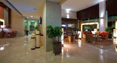 Foto del hotel Sunset Plaza Beach Resort tomada en la recepción, con decoración moderna en tonos rojizos y marrones, sillones, plantas de interior y una iluminación cálida