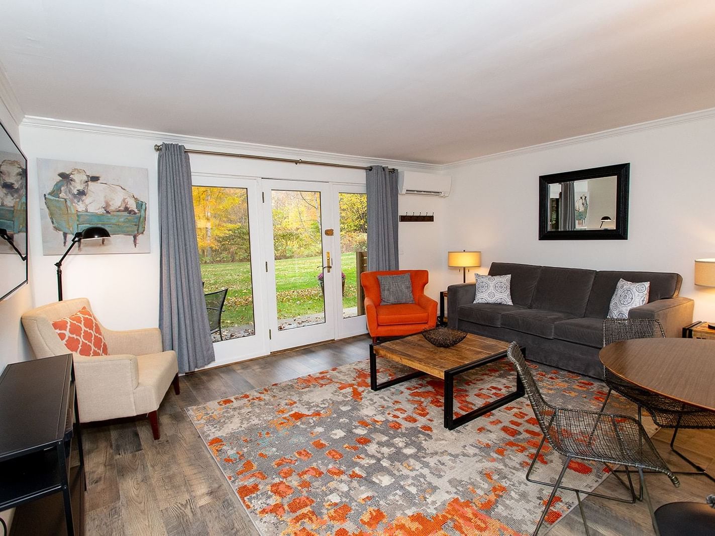 Modern living room with gray sofa, orange accent chair, and patio doors overlooking autumn foliage at Topnotch Stowe Resort.