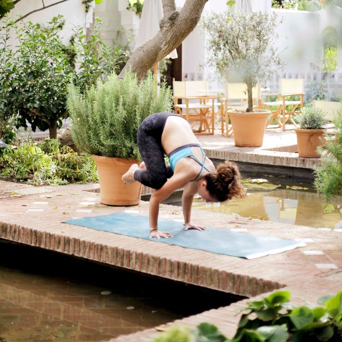 Mujer practicando postura invertida de yoga en jardín con árboles y macetas durante Taller Animal Flow