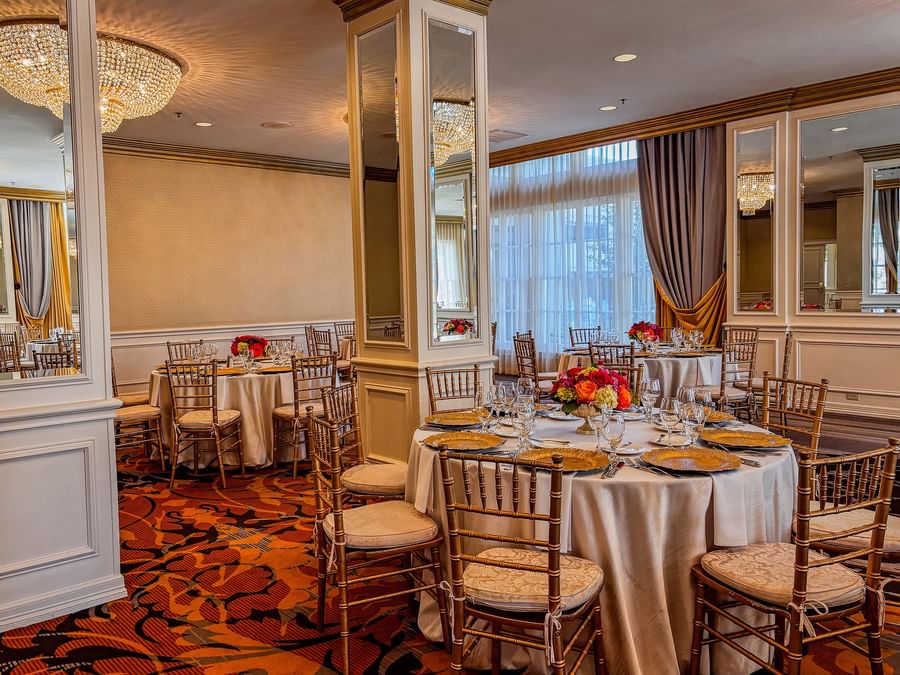 Round dining tables with gold chairs under a crystal chandelier in Crystal Ballroom at Warwick Melrose Dallas