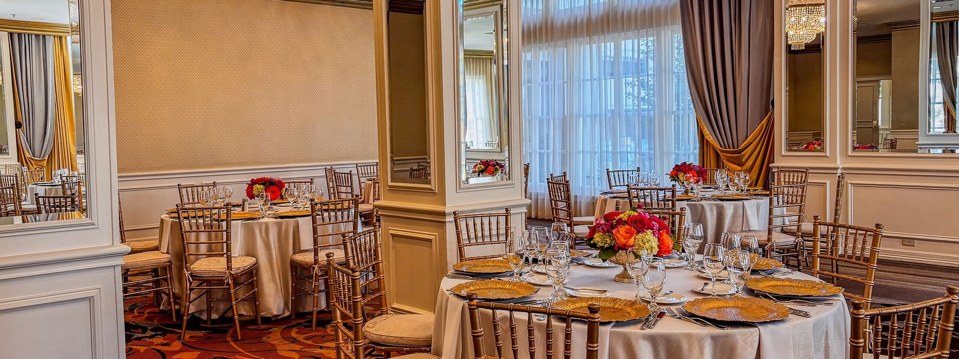 Round dining tables with gold chairs under a crystal chandelier in Crystal Ballroom at Warwick Melrose Dallas