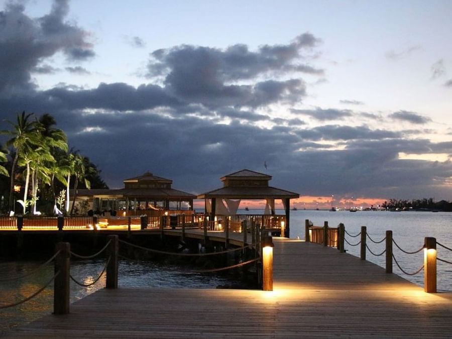 Wooden pier by gazebos under a twilight sky surrounding calm harbor water at Warwick Paradise Island Bahamas