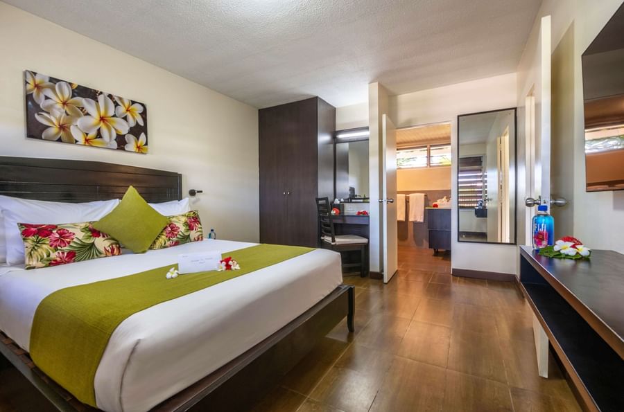 A hotel bedroom with a bed, floral decor, and wooden floors at Tokatoka Resort - Fiji International Airport.