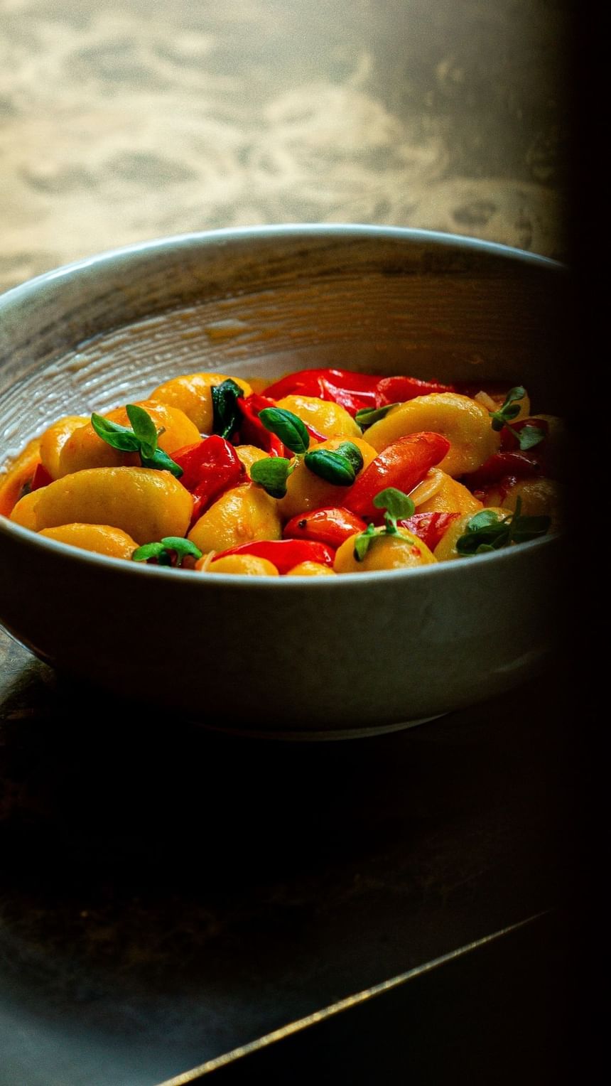 A close-up of a bowl filled with colorful gnocchi, red bell peppers, and fresh herbs at The Kitchens