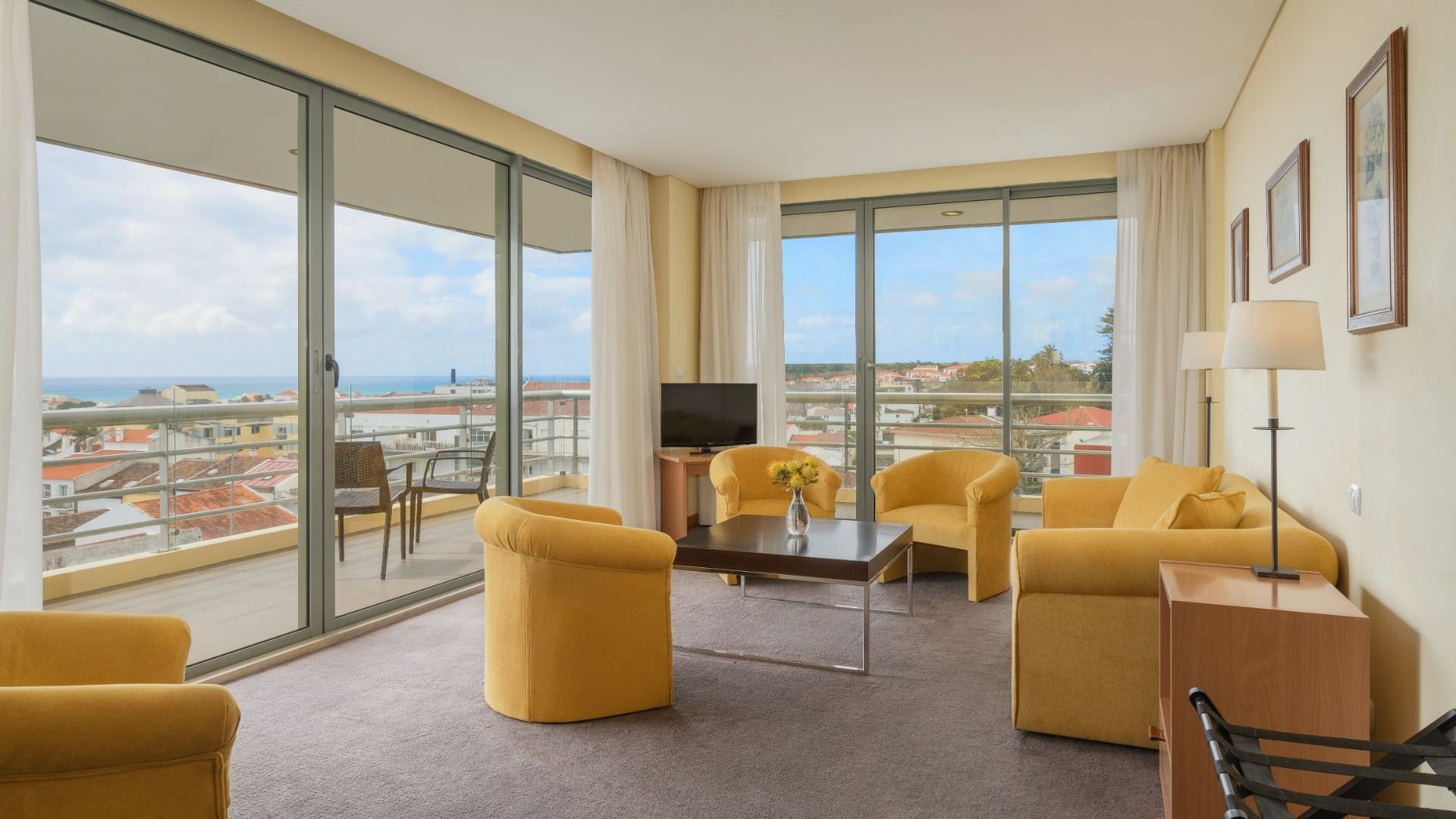 Living area with balcony access, yellow comfy chairs, TV & coffee table in a Suite at São Miguel Park Hotel