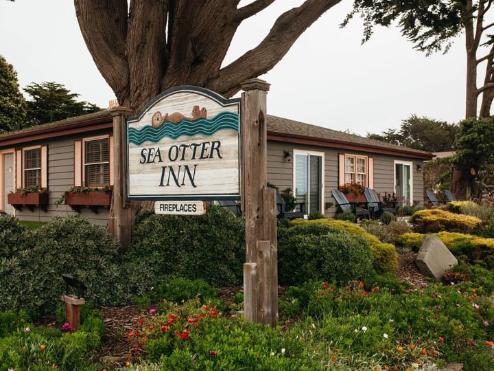 A sign reading 'Sea Otter Inn' with a tree and garden in front of a building.