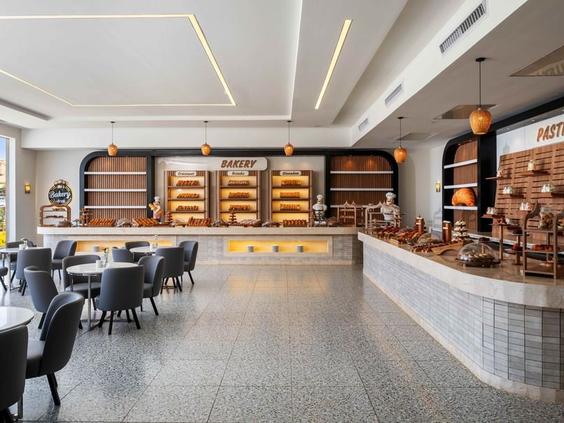 Modern bakery shop with tables and chairs, a pastry counter, and various baked goods on display.