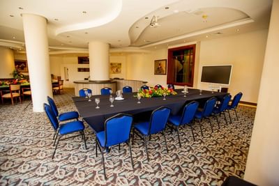 Carlton Meeting Room featuring a long table with chairs, a floral centerpiece, and a wall-mounted TV at Dann Carlton Cali