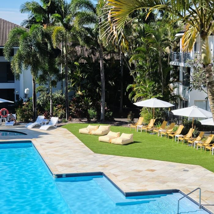 Pool area with lounge chairs, umbrellas, and palm trees in a resort setting.