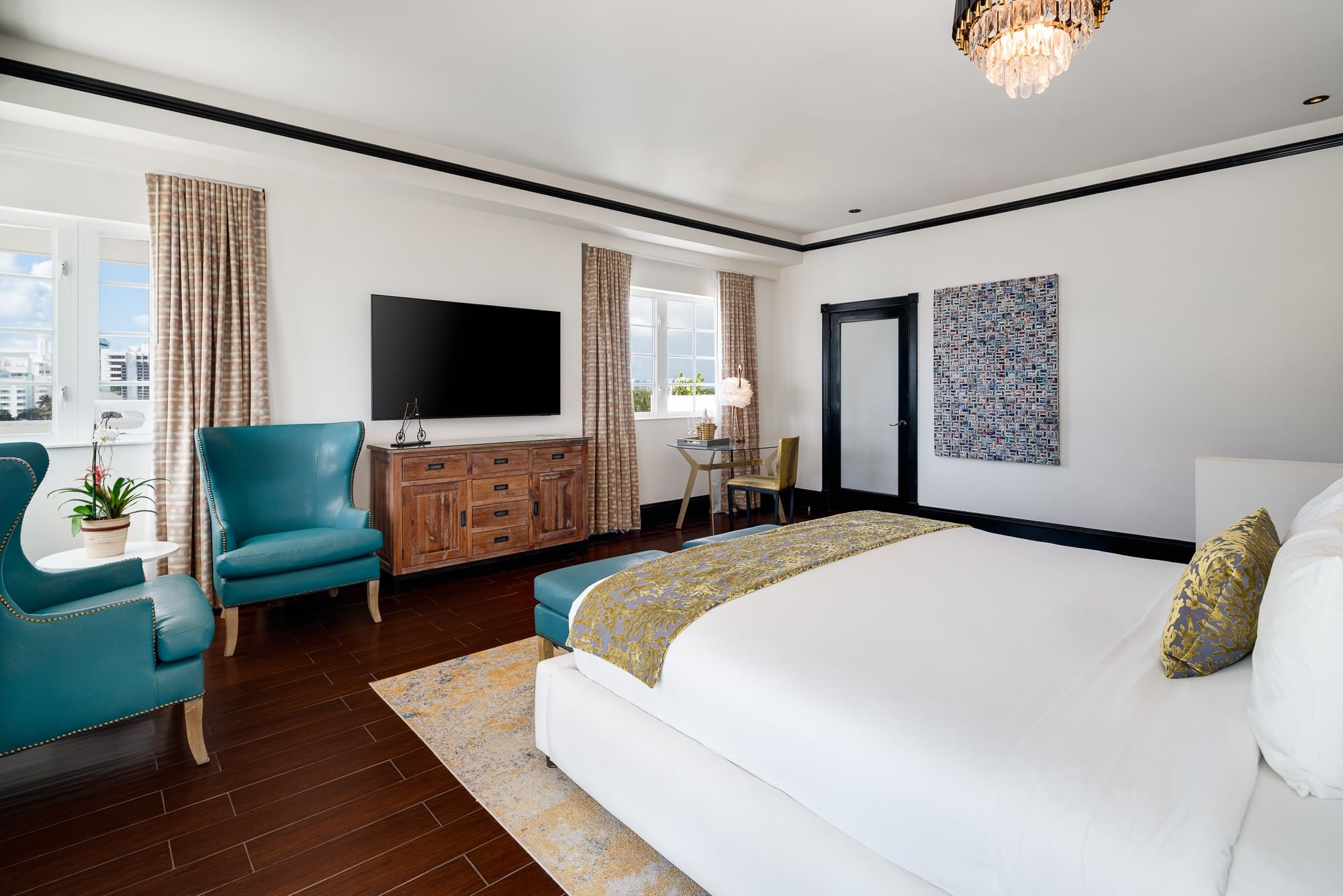 A wide view of a hotel room with a king-sized bed, TV, dresser, and chandelier.