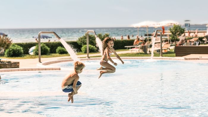 Zwei Kinder springen ins Schwimmbecken neben dem Meer bei Falkensteiner Group
