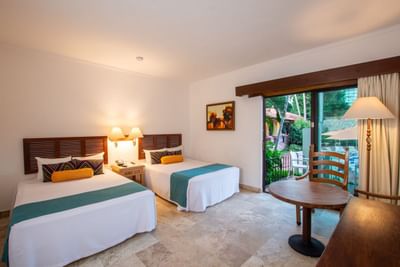 Two beds, nightstands, lamps, table, chairs, and sliding glass doors in a hotel room.