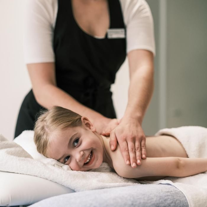 Masažna terapeutkinja radi masažu sretnom djevojčici koja leži na ležaljki.