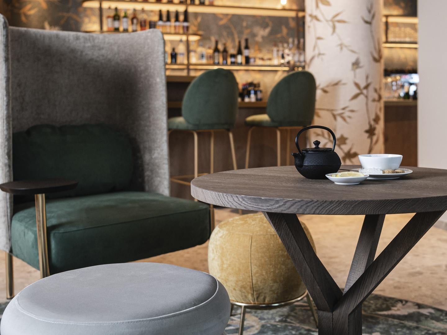 Cozy lounge area with round table, teapot, and cushioned chairs, set in a modern bar environment.