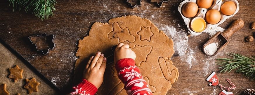 Child cutting out cookies with holiday-themed cutters and festive decor around.