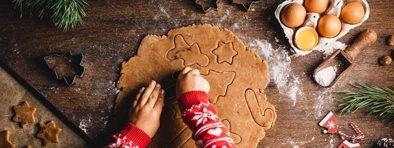 Child cutting out cookies with holiday-themed cutters and festive decor around.
