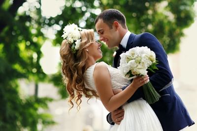 Smiling bride and groom hugging closely outdoors with a white flower bouquet at Spencer Hotel & Conference Centre