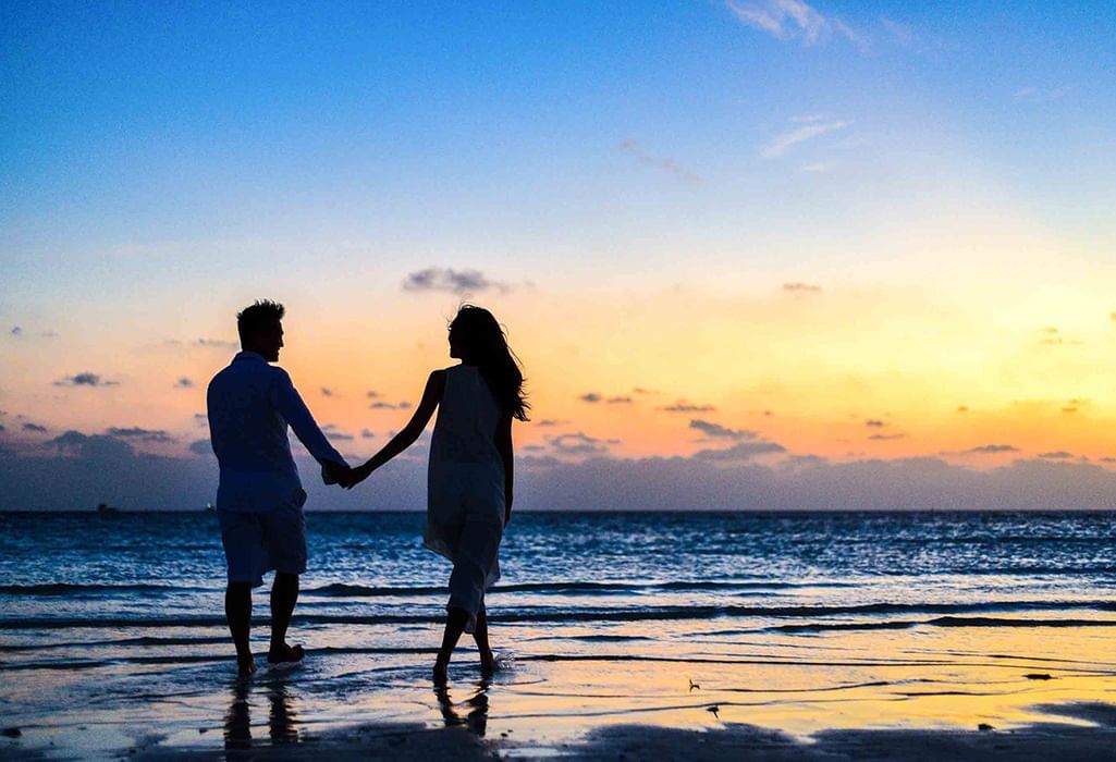 couple walking the beach hand in hand at sunset