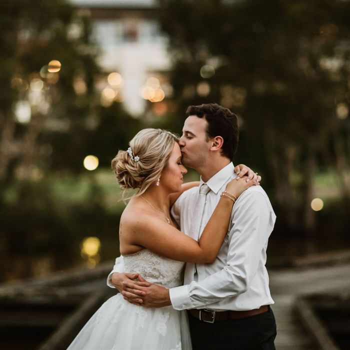 Bride and groom embrace outdoors with soft lighting in the background at Mercure Kooindah Waters