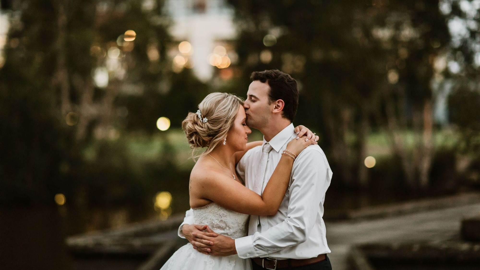 Bride and groom embrace outdoors with soft lighting in the background at Mercure Kooindah Waters