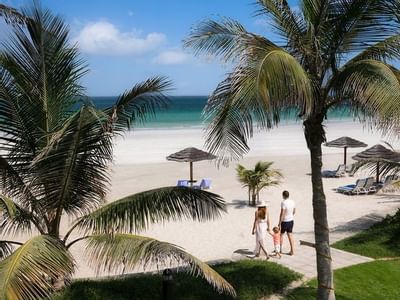 Family walking on the beach along palm trees at Ajman Hotel