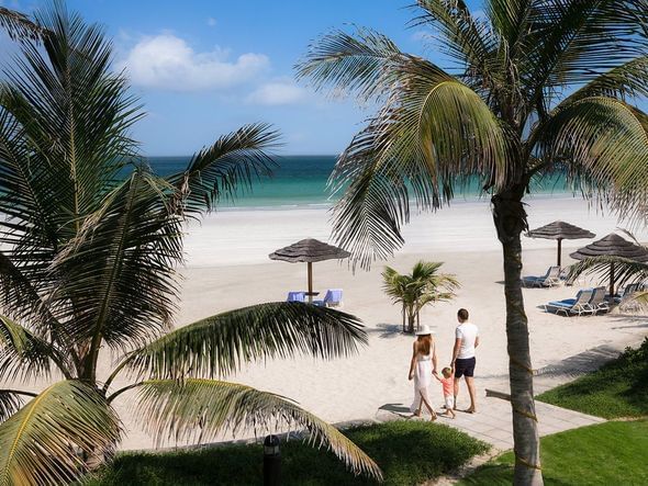 A family walking toward the white sand beach at Ajman Hotel