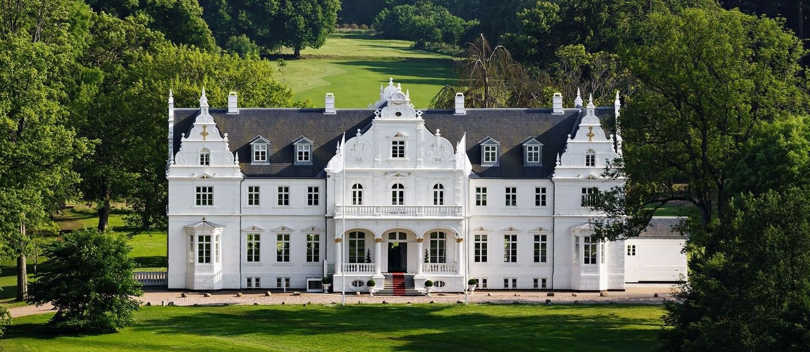 Large white estate house with green lawn and trees at Warwick Corporate