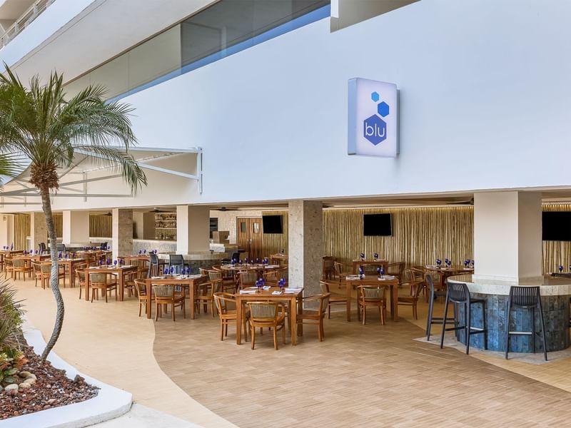Outdoor dining area with wooden tables, glassware and palm trees in Blu at Fiesta Americana Acapulco Villas