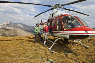 Man and woman exiting a red and white helicopter with mountains in the background near Clique Hotels & Resorts