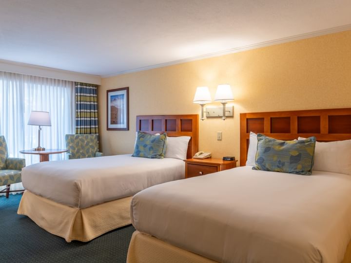 A hotel room with two beds, a window, and a seating area.