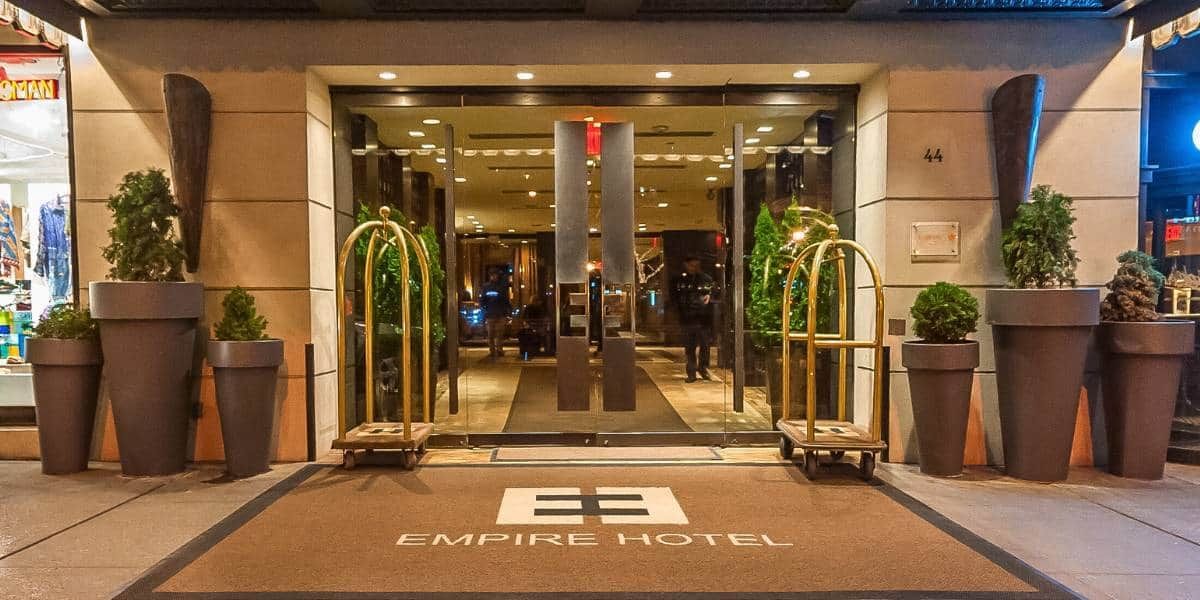 The entrance of the Empire Hotel with glass doors, luggage carts, and planters