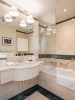 Marble vanity by a glass-enclosed bathtub under warm lights with rolled towels in Classic Room at Warwick Geneva
