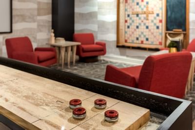 Cozy lounge area at The Riverwalk Plaza Hotel featuring a shuffleboard table, red armchairs, and a Scrabble board