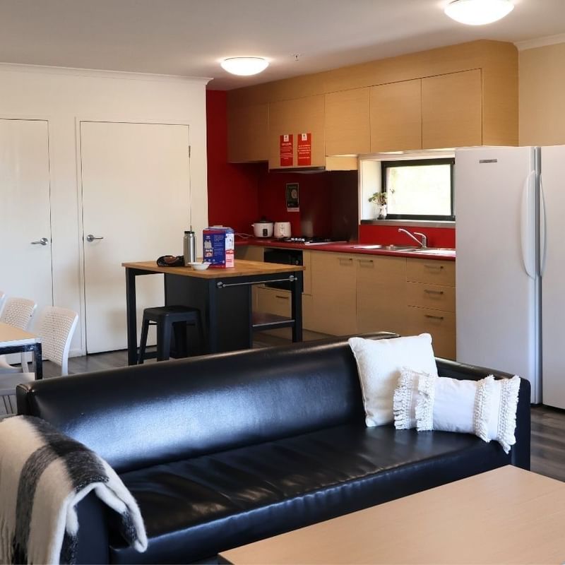 Modern living room with black leather couch, white table, and two white refrigerators at La Trobe University Hillside Apartments.