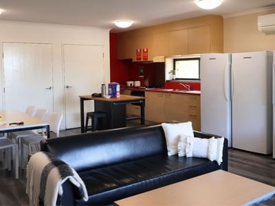 Modern living room with black leather couch, white table, and two white refrigerators at La Trobe University Hillside Apartments.