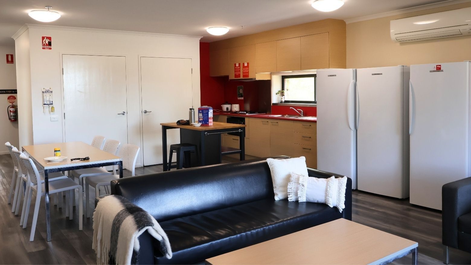 Modern living room with black leather couch, white table, and two white refrigerators at La Trobe University Hillside Apartments.