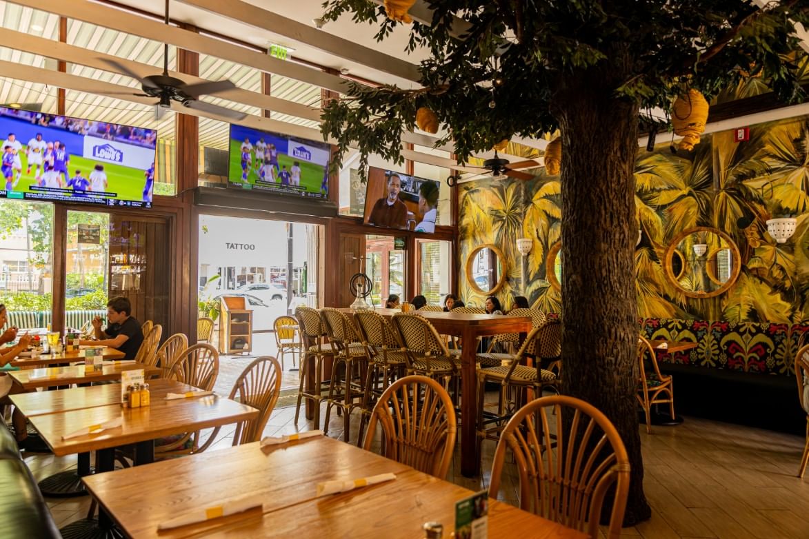 a dining area with tables and chairs, a tree, mirrors, and TVs