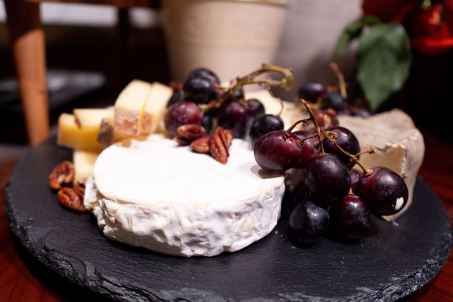 Gros plan sur un plateau de fromages composé de brie, de raisins, de noix de pécan et de tranches de fromage, présenté sur une ardoise au Warwick Paris Champs-Élysées