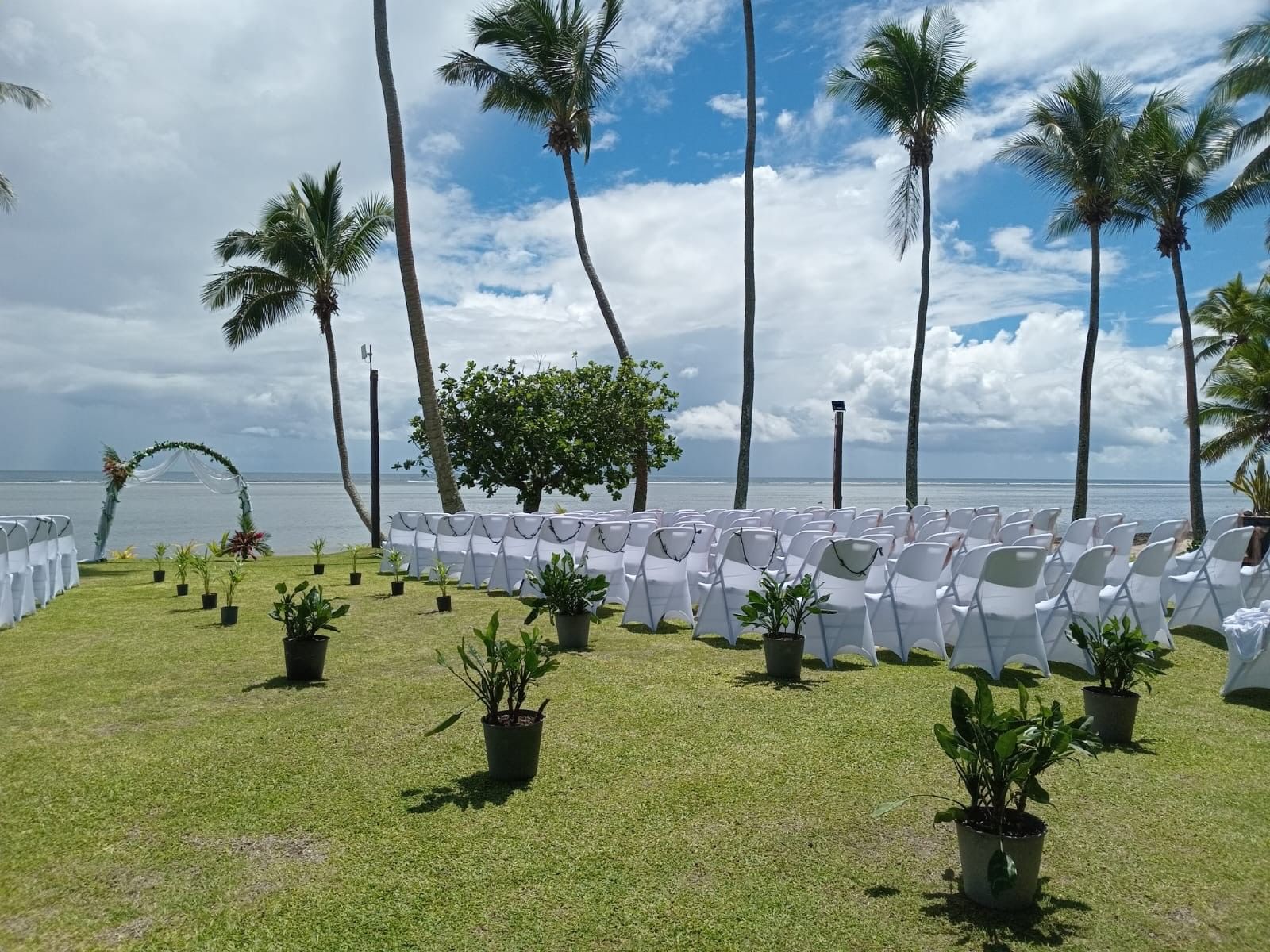 White chairs and potted plants on grassy area by the ocean under palm trees at Tambua Sands Beach Resort
