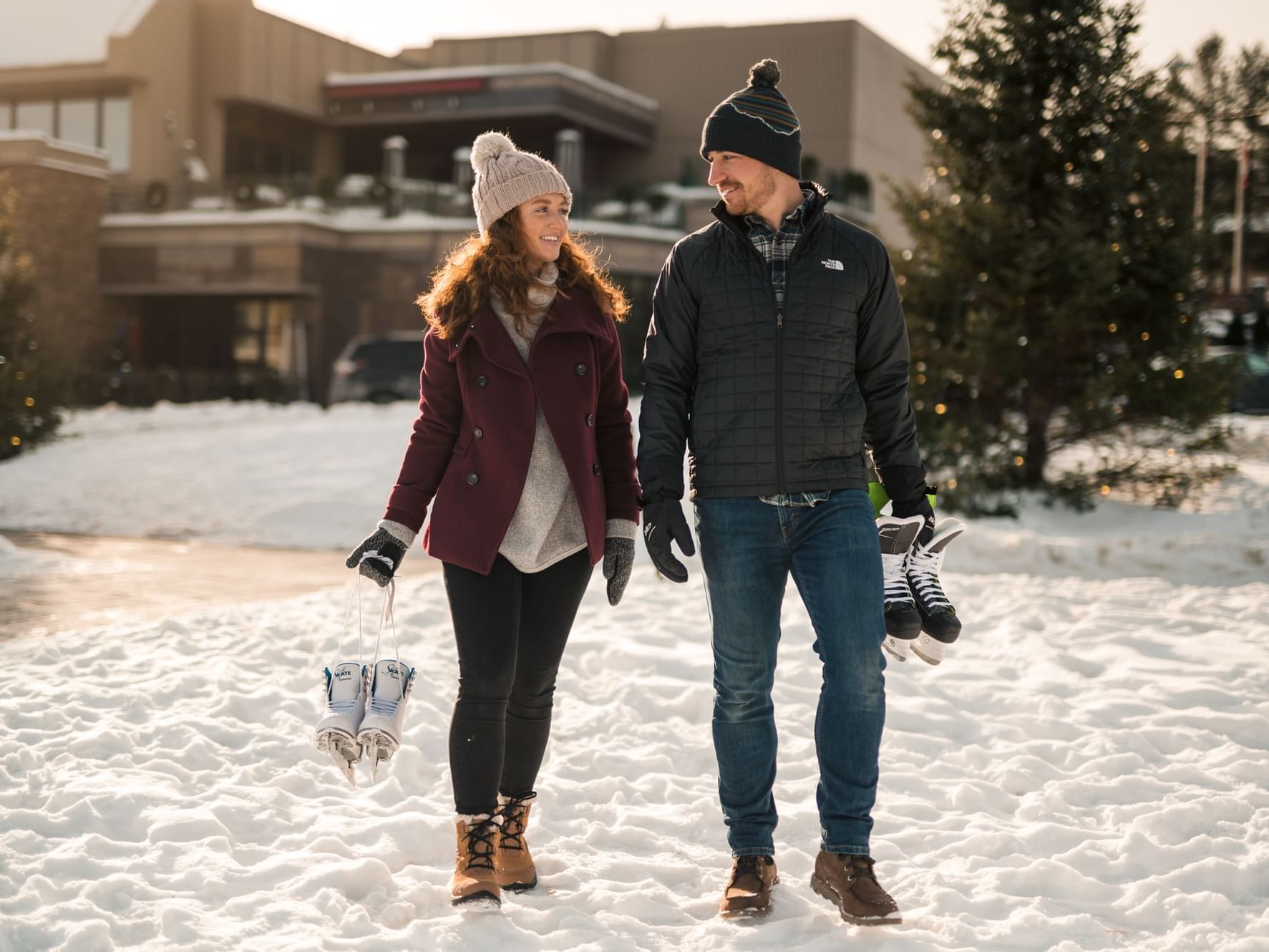 Smiling couple holding ice skates walking together on a snow-covered path at High Peaks Resort