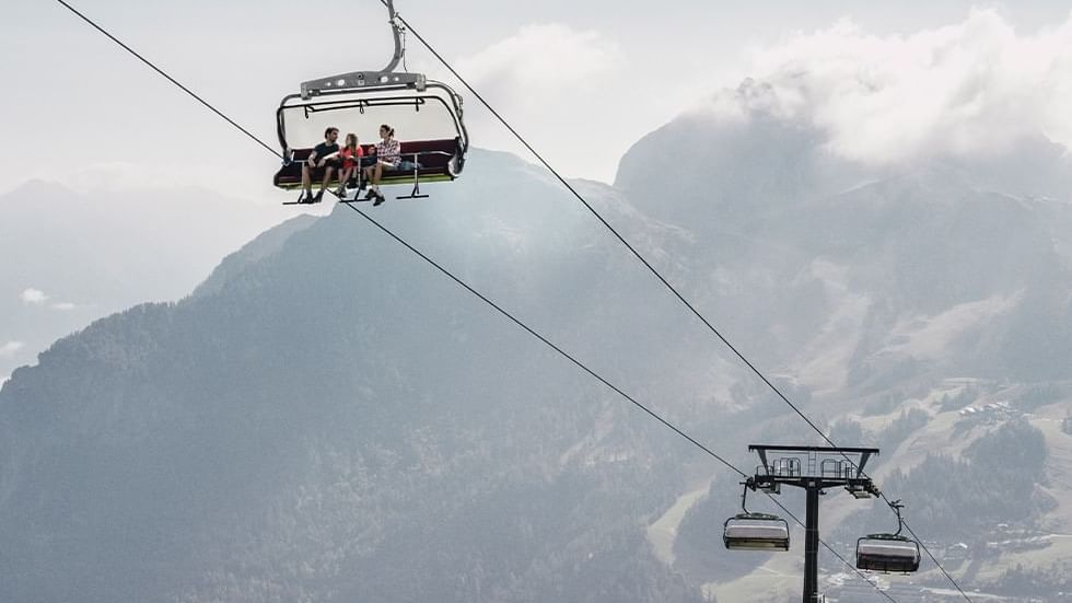 People on a chairlift with mountainous backdrop near Falkensteiner Hotel Sonnenalpe