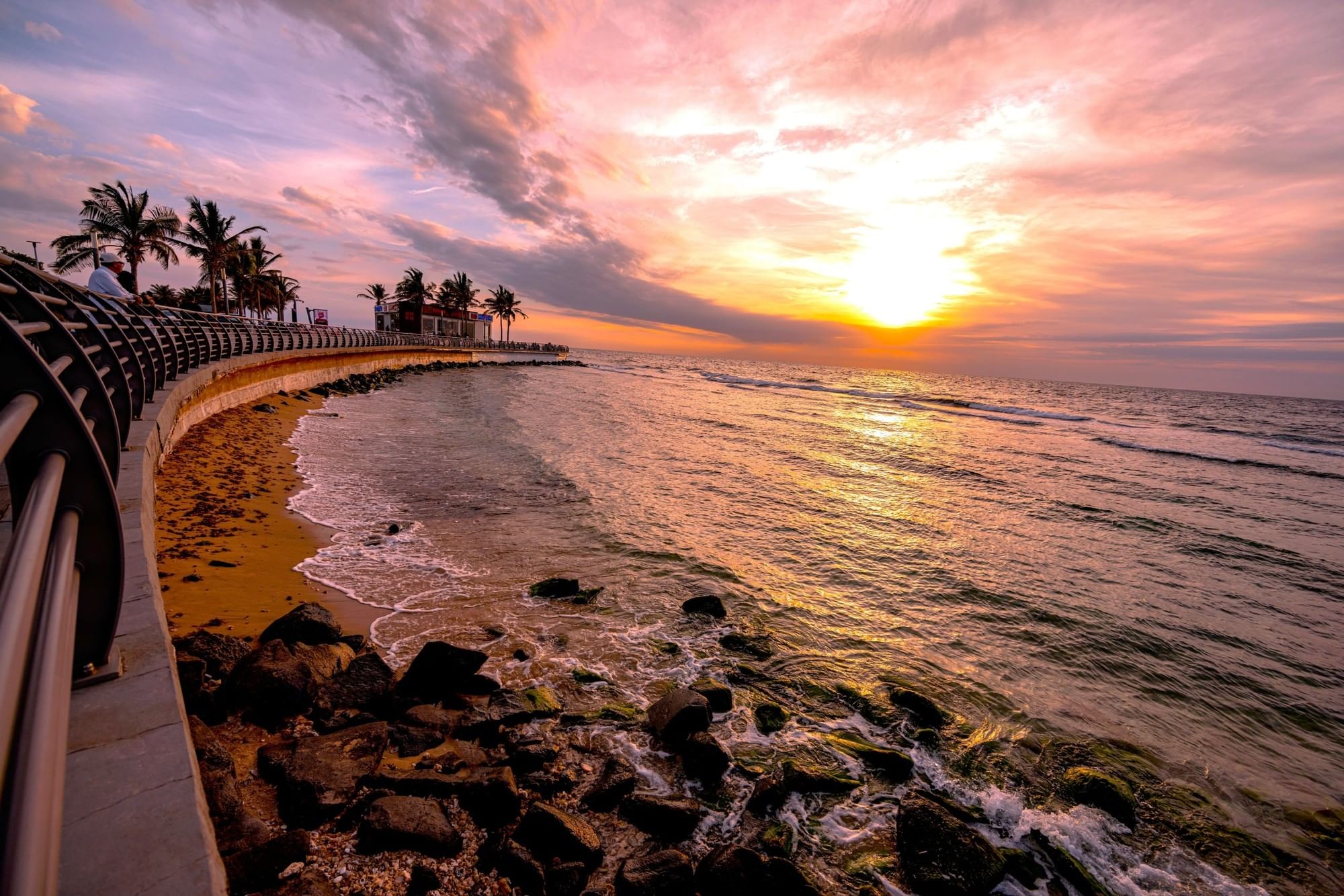 Rocky shoreline and golden sand under a vibrant pink sunset by the ocean near Warwick Al Khobar