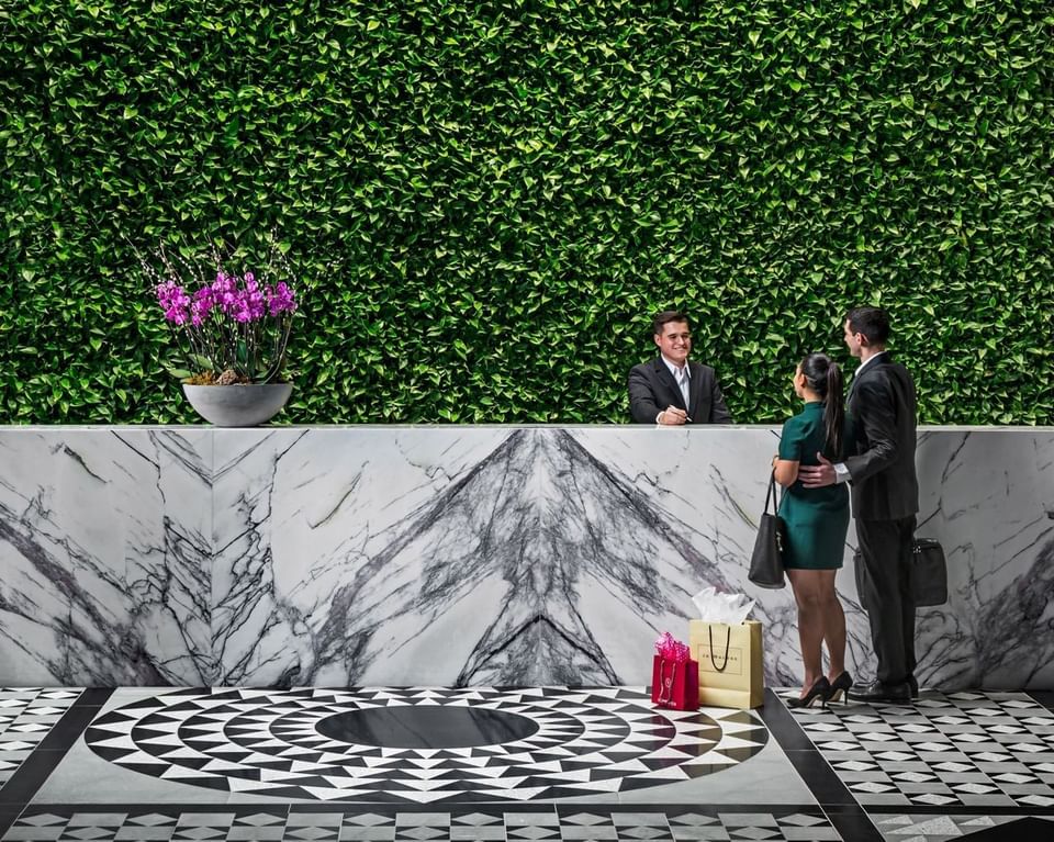 Couple standing at marble reception desk with receptionist facing living green wall and a tiled floor at Hotel X Toronto