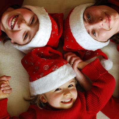 Drei Kinder in Weihnachtskleidung und Mützen liegen auf dem Boden und lächeln.
