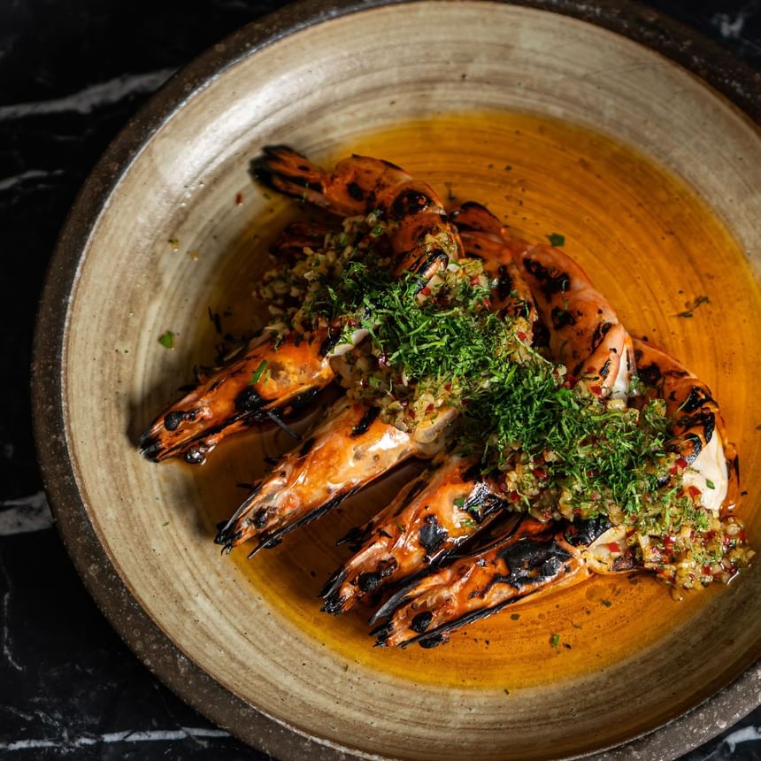 Grilled prawns with vibrant green herb topping, served in a rustic bowl at The Kitchens