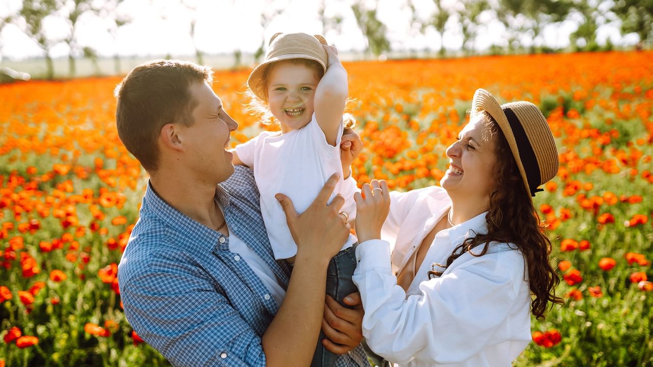 Family of three in a field of red flowers, smiling and holding each other.