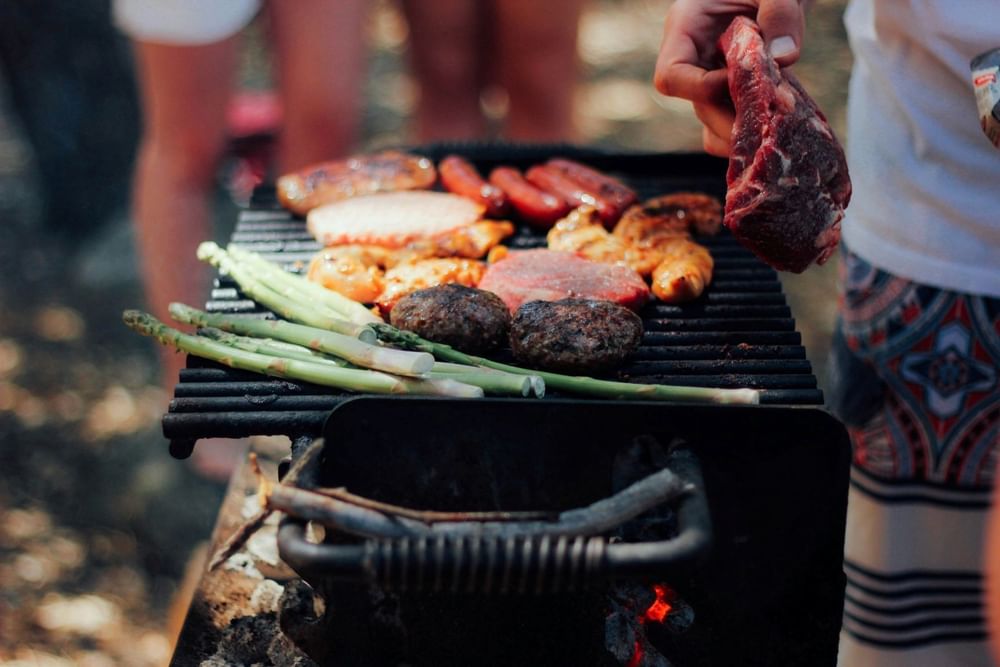 Close-up of steaks, burgers, sausages, and asparagus cooking on an outdoor grill at Shangri-La Resort and Golf Club