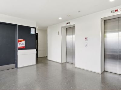 Elevators in a hallway with white walls and gray flooring at Student Living Auckland – Anzac.
